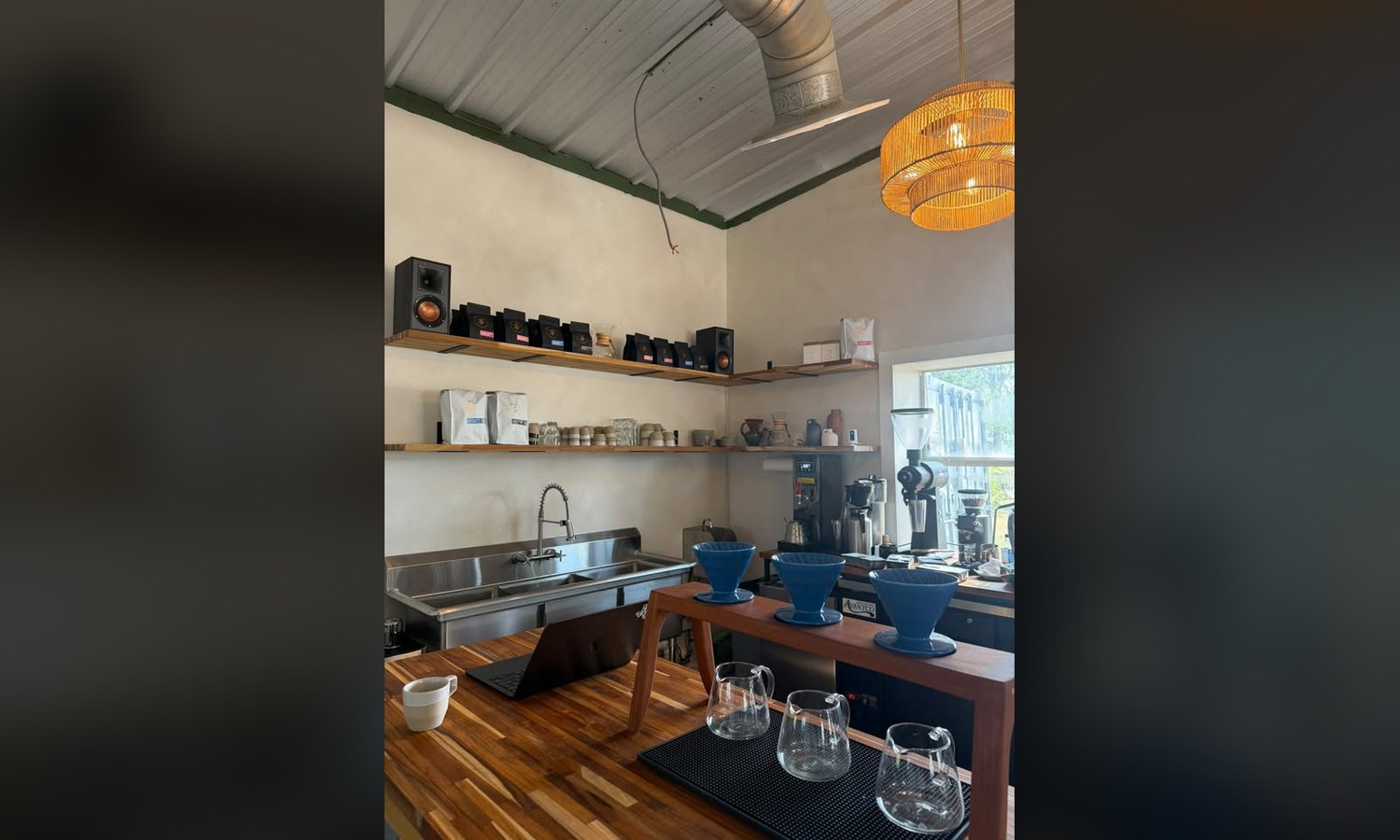 The bar runs the length of the back wall. Sink, brewer, grinders, espresso machine in the window light.